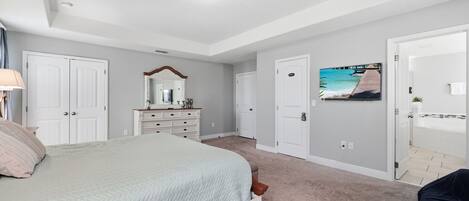 A bedroom with a bed, a dresser, a mirror, and a door leading to a bathroom.