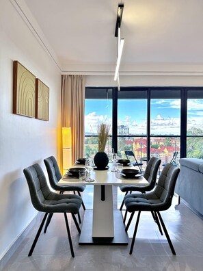 Ein moderner Essbereich mit einem Tisch für vier Personen, großen Fenstern mit Blick auf die Stadt und einer Couch im Hintergrund.