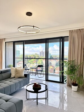 Ein modernes Wohnzimmer mit einer Couch, einem Couchtisch und Blick auf eine Stadtlandschaft durch große Fenster.