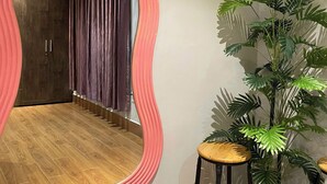 Quarto com um espelho rosa grande, piso de madeira, uma planta em vaso e uma cortina escura.