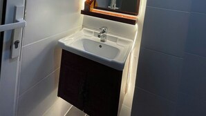 Casa de banho com lavatório branco, espelho e porta de chuveiro.