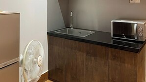 Uma cozinha compacta com armários de madeira, bancada preta, micro-ondas embutido, ventilador branco e geladeira.