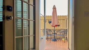 An open door leading to a balcony with a table and chairs, a pink umbrella, and a wooden fence in the background. - Horizon South 81B Resort Stay (Panama City Beach)