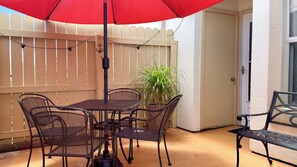 A patio with a table and chairs, a red umbrella, and a potted plant. - Horizon South 81B Resort Stay (Panama City Beach)