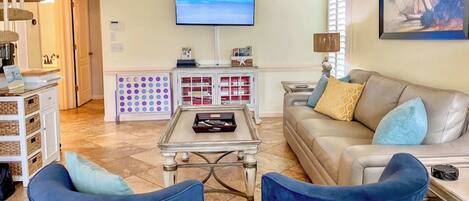 Un salon comprenant un canapé, deux fauteuils, une table basse, un téléviseur, un meuble avec des tiroirs et un tableau accroché au mur.