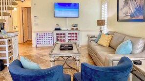 Ein Wohnzimmer mit einer Couch, zwei Sesseln, einem Couchtisch, einem Fernseher, einer Kommode und einem Bild an der Wand.