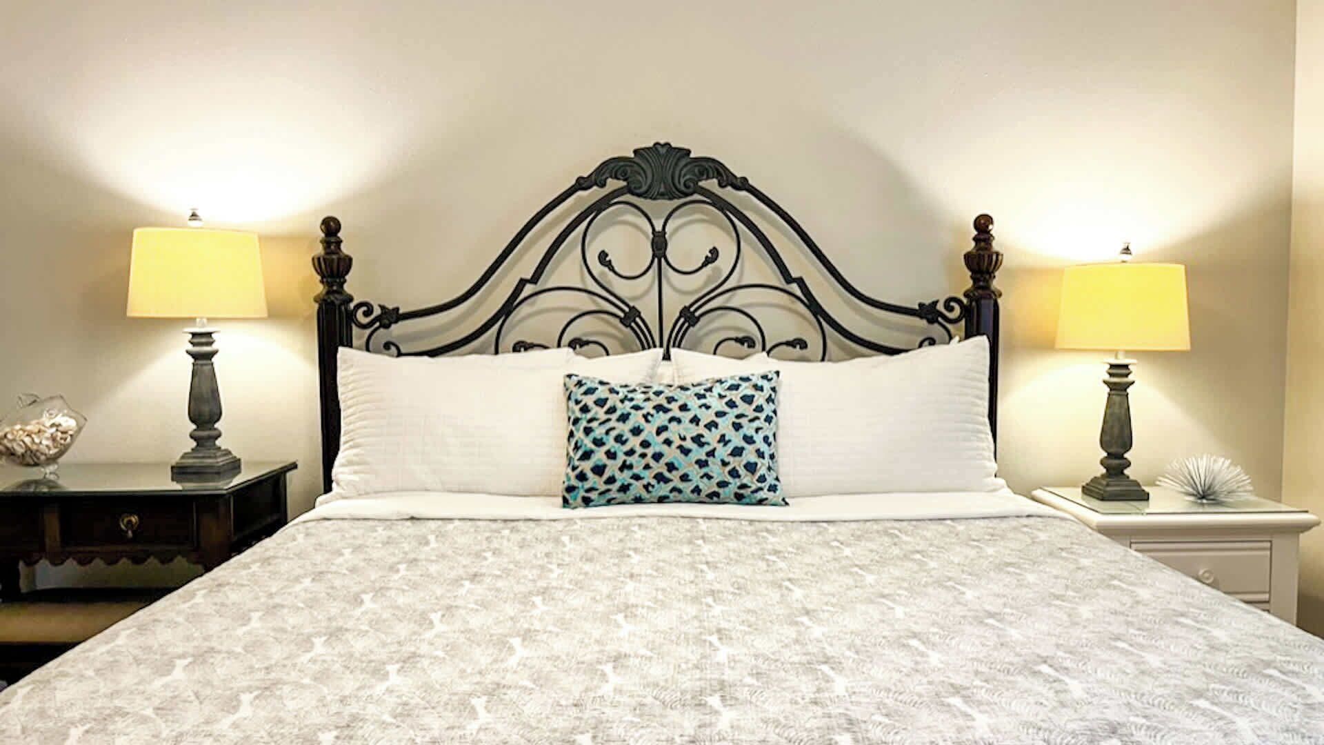 Un letto con una coperta a motivi, un cuscino decorativo e due lampade ai lati.