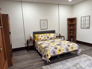 A bedroom with a bed, nightstands, a wooden wardrobe, a bookshelf, and a framed picture on the wall.