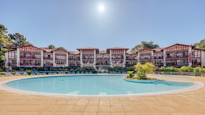 Un hotel con una piscina grande, varios balcones y cielo despejado.