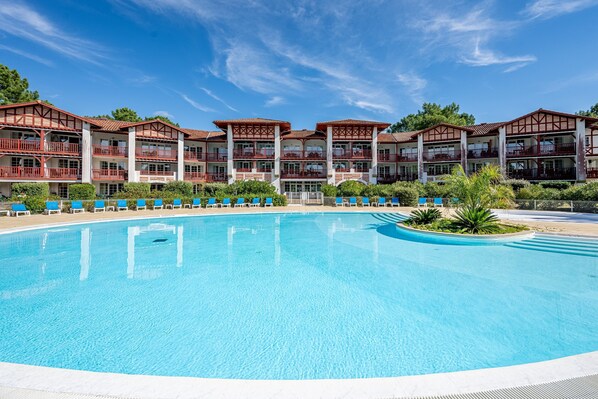 A large swimming pool with blue water, surrounded by a building with multiple balconies and a clear blue sky. - Stunning Landes Pine Apartment for 5 (Biscarrosse)