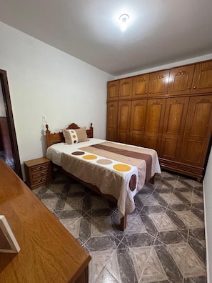 Quarto com cama, guarda-roupa de madeira e soalho em azulejos.