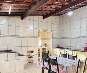 A kitchen with tiled walls, a dining table with chairs, a fruit basket, and a stove.