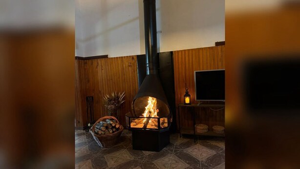 Una estufa de leña con fuego, un televisor y una cesta de leña.