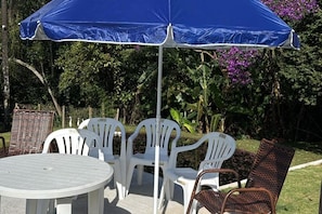 Uma mesa redonda com cadeiras brancas e um guarda-sol azul.
