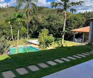 Piscina rodeada por um gramado com um alpendre e um edifício ao fundo.