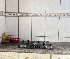Una cocina con estufa a gas, un tazón rojo y una botella de aceite sobre la encimera.