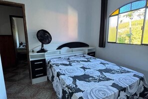 Un dormitorio con cama, mesita de noche, espejo y ventana con vistas a zonas verdes.