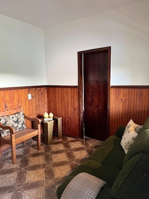 Una habitación con un banco de madera, un sofá verde, una mesita con un jarrón y una puerta de madera.