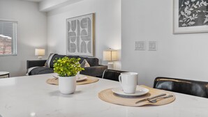 Ein moderner Essbereich mit einem weißen Tisch, gedeckt für zwei Personen, einem Blumentopf und einem großen abstrakten Kunstwerk an der Wand.