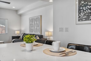 Ein moderner Essbereich mit einem weißen Tisch für zwei Personen, einem Blumentopf und einem großen abstrakten Kunstwerk an der Wand.