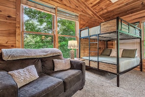 Ein Holzblockhaus im Inneren mit einem Etagenbett, einer Couch mit Kissen und großen Fenstern.