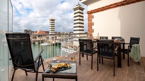A balcony with a table set for two, chairs, and a view of the marina with boats and buildings. - Premium Deauville Spa Apartment for 8 (Deauville)