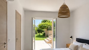 A bedroom with a bed, a bedside table, a lamp, a hanging light fixture, and a view of a garden through an open door. - Fully renovated villa in Provence, with large pool and spectacular valley view (Bargemon)