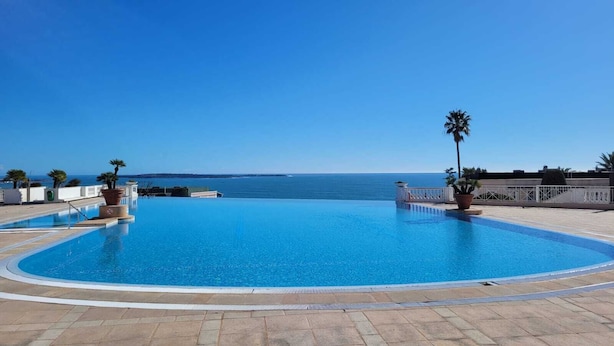 A clear blue infinity pool with a view of the sea, surrounded by a tiled deck and palm trees. - L'Ecrin Lolita Cannes - Exceptional (Cannes)