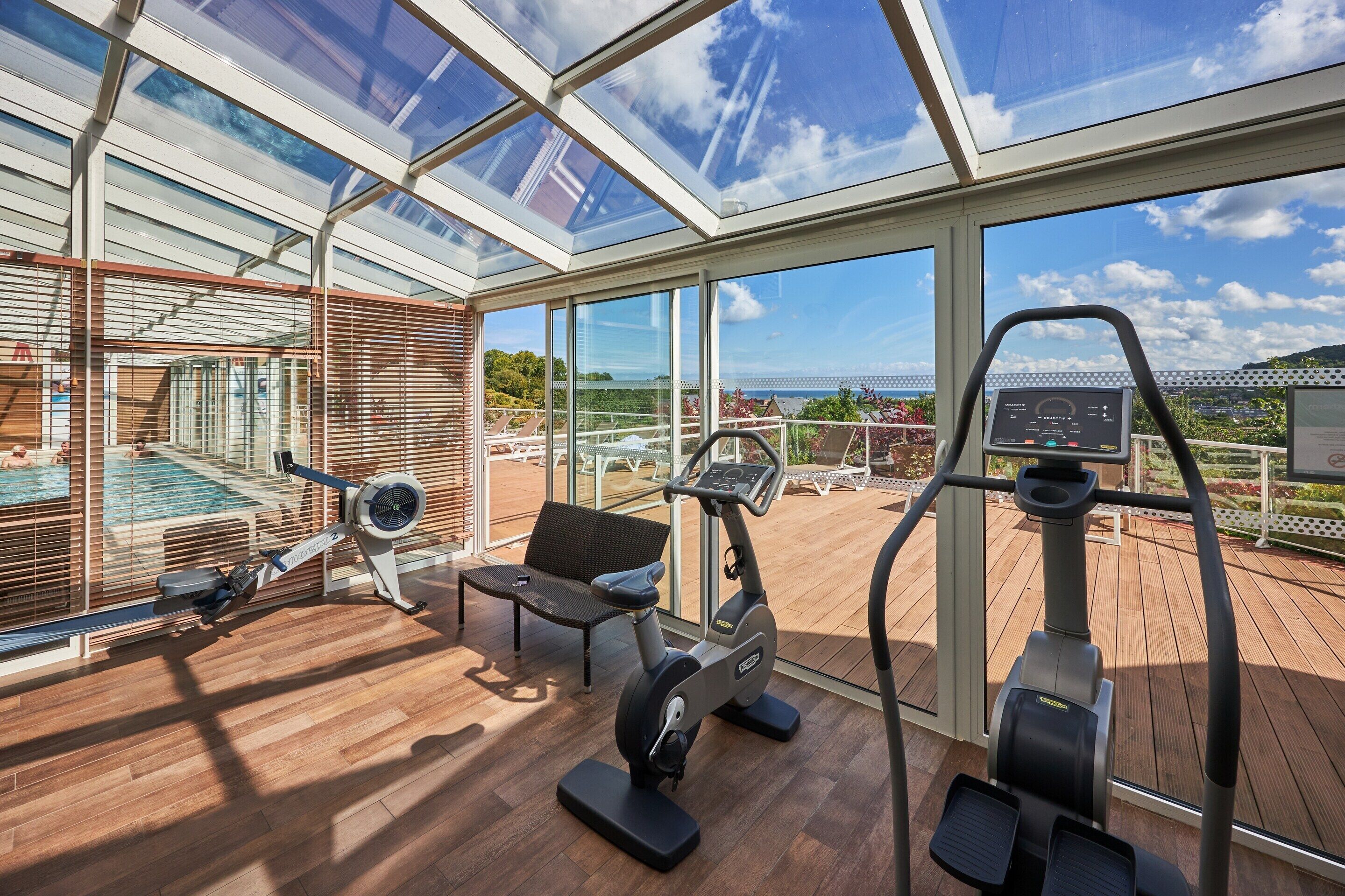 A gym with exercise equipment, a bench, and a view of a pool and greenery.