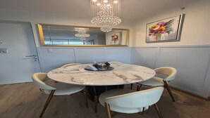 A dining area with a round table, four chairs, a chandelier, a mirror, and a floral painting on the wall. - Modern Apt in Lince Just Steps from San Isidro (Lince)