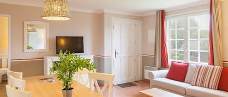 Ein Wohnzimmer mit einer Couch, einem Esstisch mit Stühlen, einem Fernseher und einer Topfpflanze.