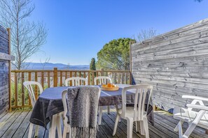 Un área de comedor al aire libre con una mesa y sillas, una terraza de madera y vistas a montañas.