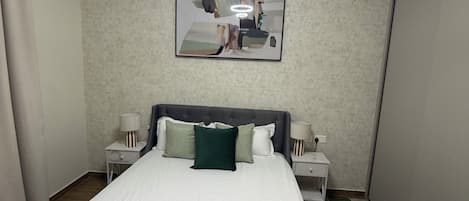 Een moderne slaapkamer met een groot bed, twee nachtkastjes, een spiegel en een plafondlamp.