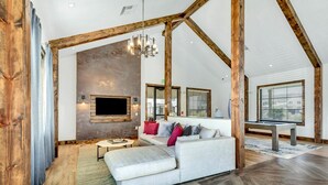 A loft-style living room with exposed wooden beams, a large sofa, a TV mounted on the wall, and a dining table. - Landing | Spectacular 1BD, Gym, Pool (Madison)