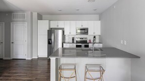 A modern kitchen with white cabinetry, stainless steel appliances, and a large island with bar stools. - Landing | Spectacular 1BD, Gym, Pool (Madison)