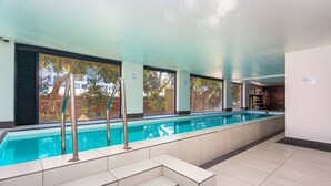 An indoor swimming pool with clear glass walls, steps leading into the pool, and a view of the outside. - Mountain Views 2BR Furnished De Waterkant (Cape Town)