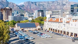 A parking lot with multiple cars, a building with solar panels, and a mountainous backdrop. - Mountain Views 2BR Furnished De Waterkant (Cape Town)