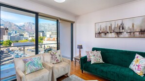 A modern living room with a sofa, two armchairs, a painting, and a view of a cityscape through large windows. - Mountain Views 2BR Furnished De Waterkant (Cape Town)
