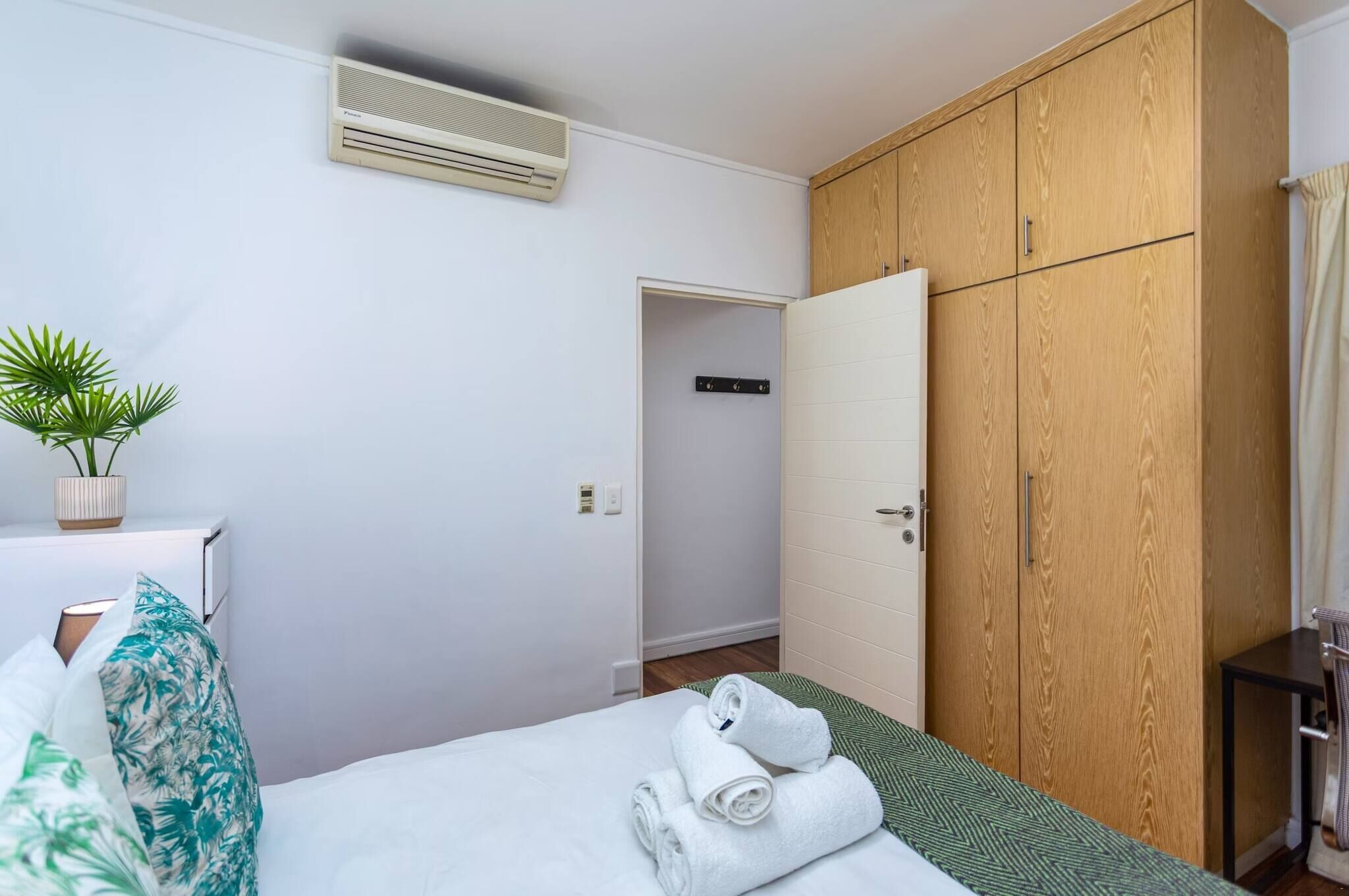 Quarto de hotel com cama, um guarda-roupa de madeira, uma planta em vaso e aparelho de ar condicionado.