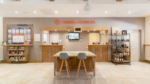 Zona de recepción con un mostrador de madera, dos taburetes, un televisor y una estantería con diversos objetos.