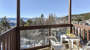 Un balcón con mesa y sillas, con vistas a un paisaje nevado de montañas y árboles.
