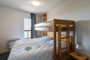 A bunk bed with a headboard, a bedside table with a lamp, a window with curtains, and a radiator. - Pyrenees Alpine Apartment for 5 (Font-Romeu-Odeillo-Via)