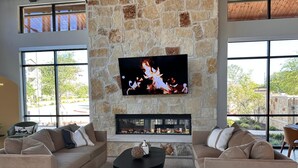 Una sala de estar con paredes de piedra, un televisor de pantalla plana, una chimenea y dos sofás con cojines.