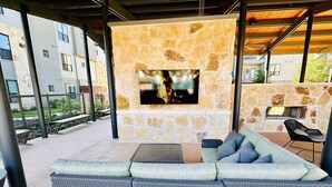 Un área de estar al aire libre con chimenea de piedra, un televisor de pantalla plana y un sofá acolchado.