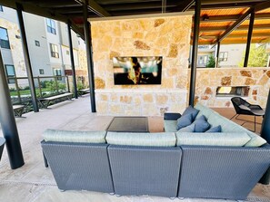 Un área de estar al aire libre con chimenea de piedra, un televisor de pantalla plana y un sofá de fibras naturales.