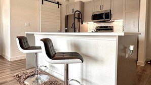 Una cocina moderna con una isla central, taburetes de bar, iluminación colgante y electrodomésticos de acero inoxidable.