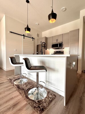 Una cocina moderna con una isla central, taburetes de bar, lámparas colgantes y electrodomésticos de acero inoxidable.