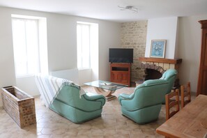 Ein Wohnzimmer mit zwei türkisblauen Sesseln, einem Glastisch, einem Fernseher auf einem Holzboden und einem Kamin.