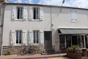 Ein zweigeschossiges Gebäude mit weißen Fensterläden, ein Fahrrad vor der Tür und ein Laden mit Beschilderung.