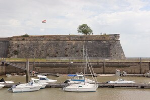 Ein Hafen mit vertäuten Booten, eine Flagge auf einem Fahnenmast und eine hohe Festungsmauer im Hintergrund.